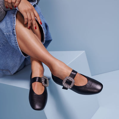 Black shoes with embellishments worn by a person sitting on a geometric blue surface